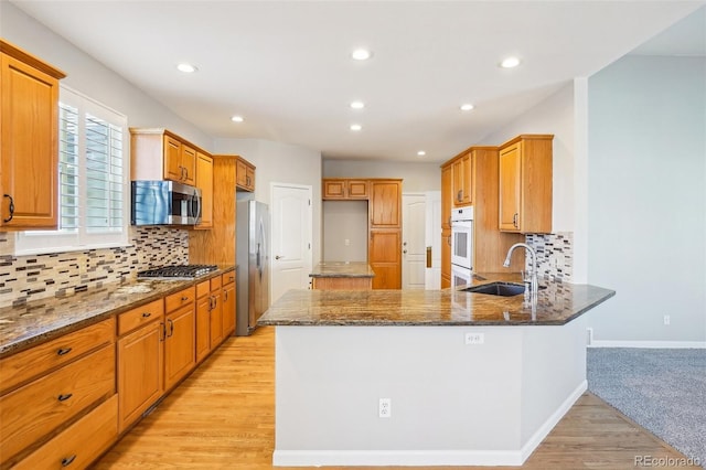 17309 Witten Ct, Parker, CO 80134 - kitchen featuring a peninsula, light wood-type flooring, dark stone countertops, a sink, and stainless steel appliances