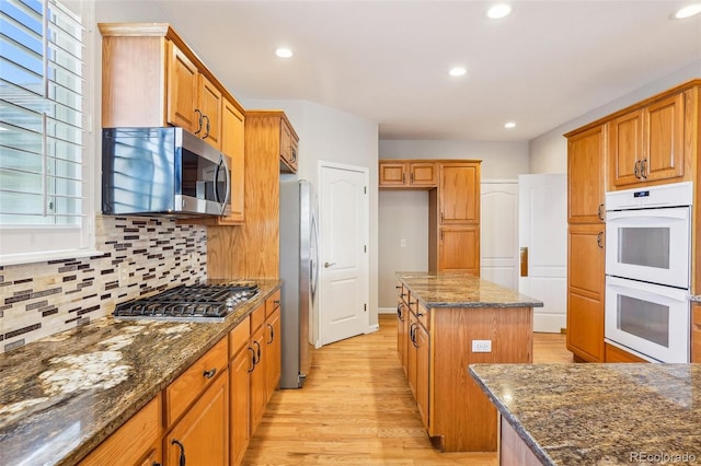 17309 Witten Ct, Parker, CO 80134 - kitchen with light wood-style flooring, a kitchen island, dark stone counters, decorative backsplash, and stainless steel appliances