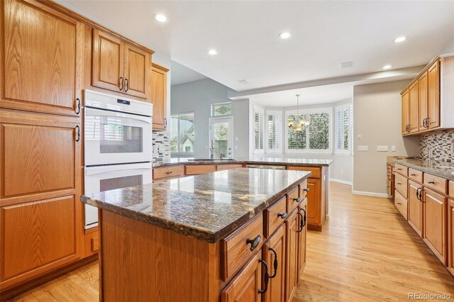 17309 Witten Ct, Parker, CO 80134 - kitchen featuring a center island, a peninsula, double oven, light wood finished floors, and decorative backsplash