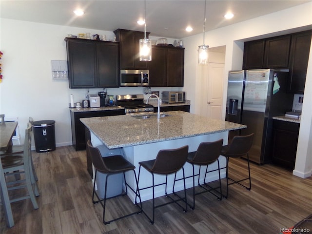 kitchen with stainless steel appliances, a kitchen island with sink, sink, decorative light fixtures, and dark hardwood / wood-style floors