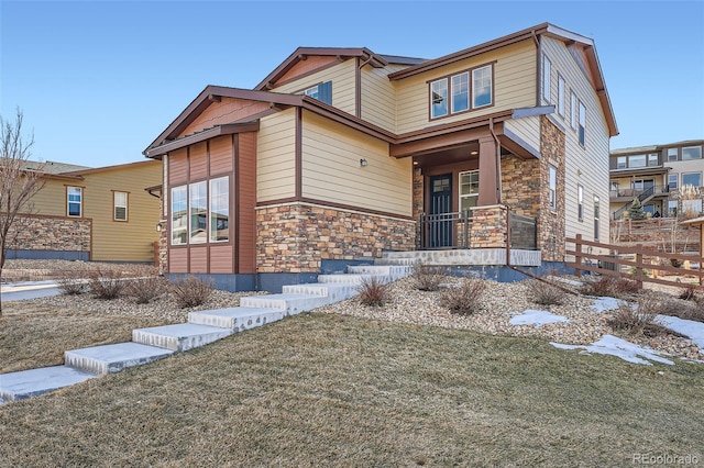 craftsman inspired home with stone siding, a porch, a front yard, and fence