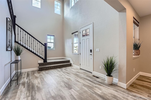 foyer entrance with a wealth of natural light, stairs, baseboards, and wood finished floors