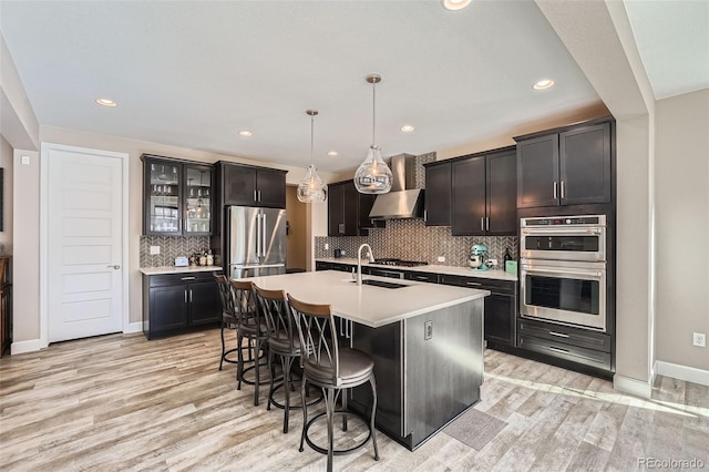 kitchen with appliances with stainless steel finishes, light wood-style floors, a sink, a kitchen breakfast bar, and extractor fan