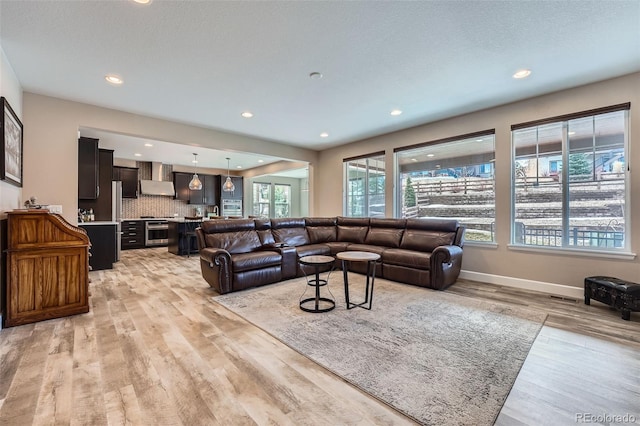 living area featuring light wood-type flooring, baseboards, a textured ceiling, and recessed lighting