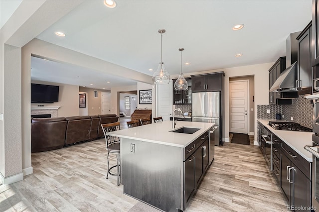 kitchen with light wood-style floors, wall chimney exhaust hood, appliances with stainless steel finishes, and a breakfast bar