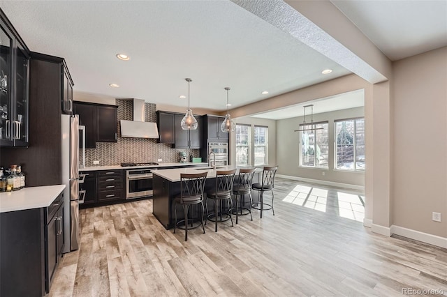 kitchen featuring backsplash, a kitchen breakfast bar, light countertops, wall chimney range hood, and a sink