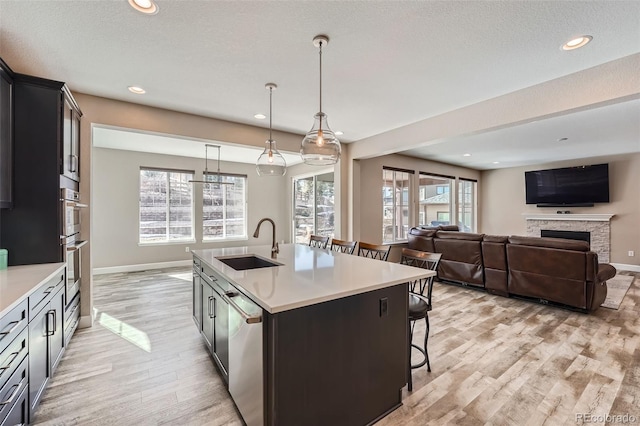 kitchen with a fireplace, a sink, light countertops, appliances with stainless steel finishes, and a kitchen bar