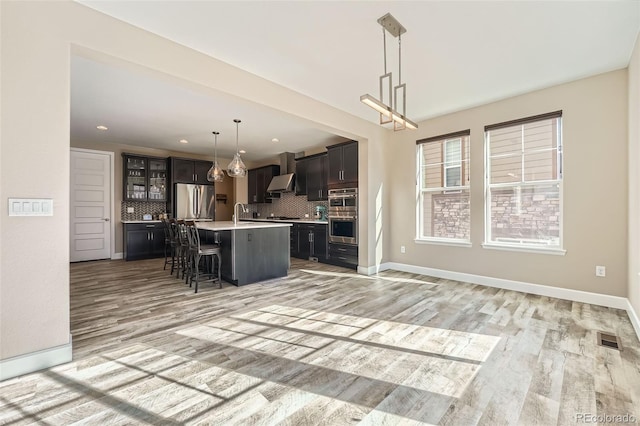 kitchen with visible vents, a kitchen breakfast bar, light countertops, appliances with stainless steel finishes, and wall chimney exhaust hood