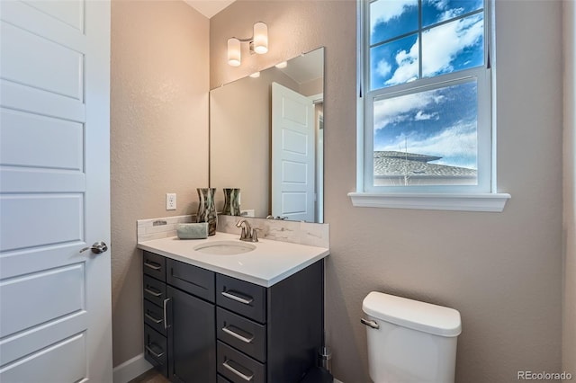 bathroom with toilet, a textured wall, and vanity