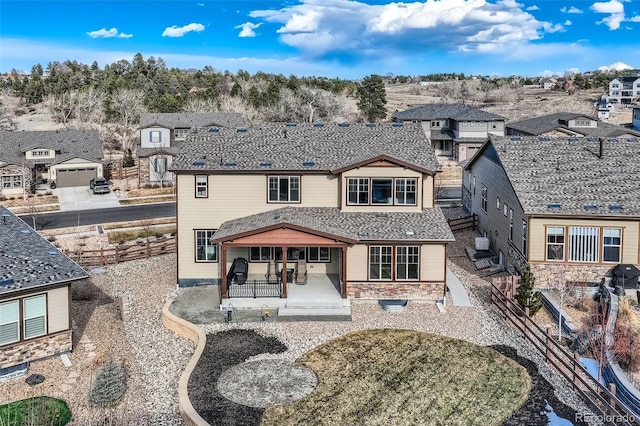 view of front of home featuring a shingled roof, a patio, stone siding, a residential view, and fence