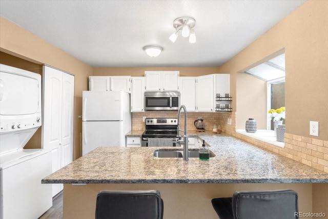 18131 E Arizona Ave Unit B, Aurora, CO 80017 - kitchen featuring stainless steel appliances, stacked washer / drying machine, a peninsula, backsplash, and white cabinetry