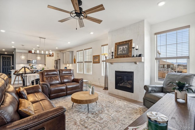 living area with light wood-type flooring, a ceiling fan, recessed lighting, a fireplace, and baseboards