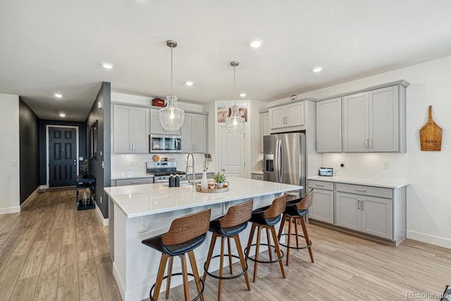 kitchen featuring a kitchen bar, gray cabinets, appliances with stainless steel finishes, and light wood-type flooring