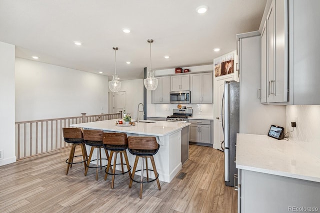 kitchen featuring light wood-type flooring, gray cabinets, appliances with stainless steel finishes, a kitchen breakfast bar, and a kitchen island with sink