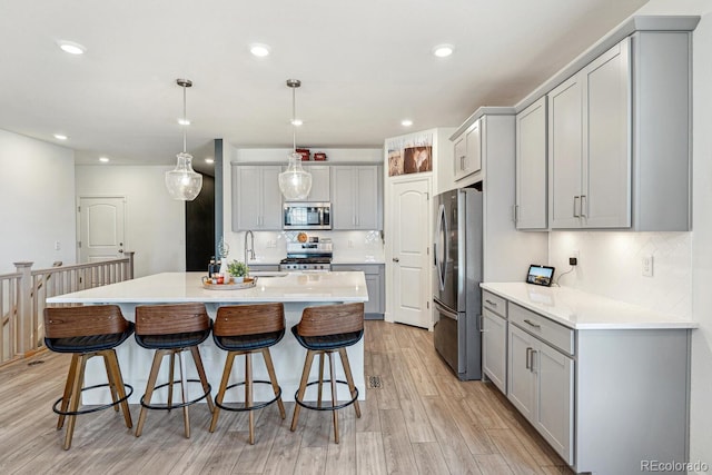 kitchen featuring decorative backsplash, gray cabinets, light wood-style floors, stainless steel appliances, and a sink