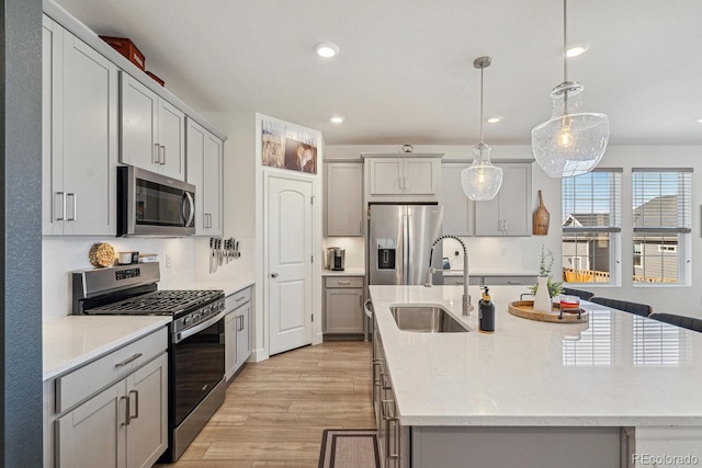 kitchen with gray cabinetry, light wood-type flooring, an island with sink, appliances with stainless steel finishes, and a sink