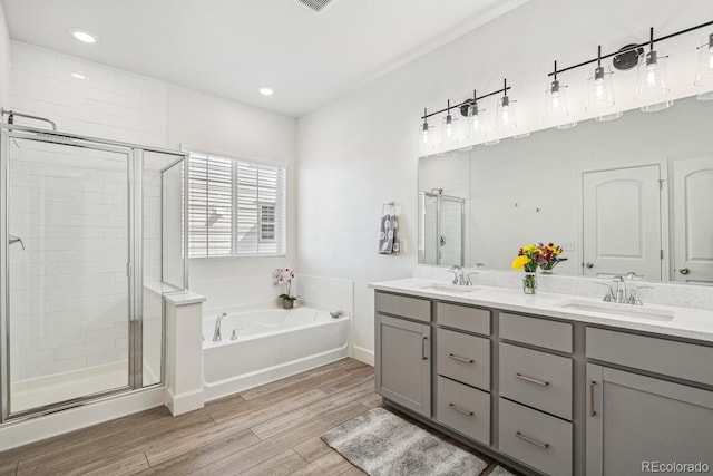 bathroom featuring a shower stall, double vanity, wood finished floors, a bath, and a sink