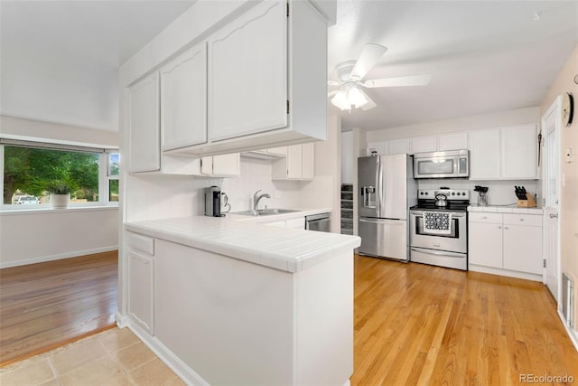 6798 Depew St, Arvada, CO 80003 - kitchen featuring appliances with stainless steel finishes, white cabinets, ceiling fan, decorative backsplash, and a peninsula