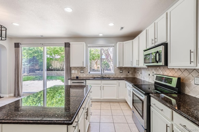 7838 W Layton Way, Littleton, CO 80123 - kitchen with appliances with stainless steel finishes, a sink, light tile patterned floors, a center island, and decorative backsplash