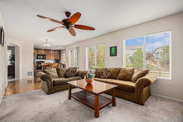 living area featuring visible vents, a ceiling fan, baseboards, light colored carpet, and arched walkways