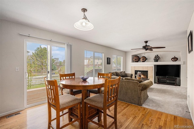 dining room with ceiling fan, a fireplace, light wood-type flooring, and visible vents