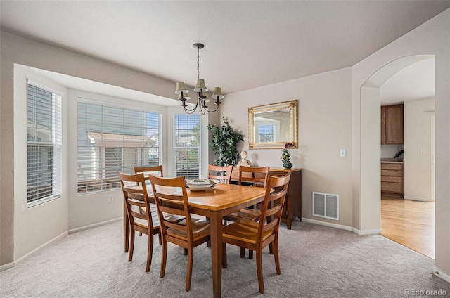 dining space with visible vents, baseboards, light colored carpet, a chandelier, and arched walkways