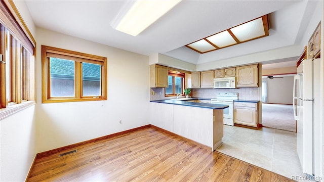 kitchen featuring a peninsula, white appliances, backsplash, and a wealth of natural light