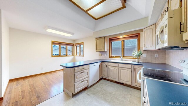 kitchen featuring backsplash, a sink, white appliances, a peninsula, and baseboards