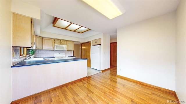 kitchen featuring a peninsula, white appliances, a sink, decorative backsplash, and light wood finished floors