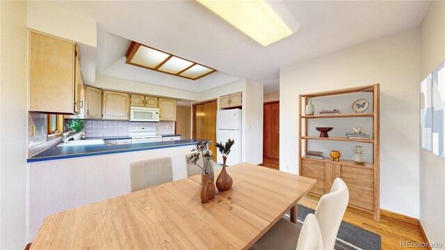 kitchen featuring a peninsula, white appliances, a sink, light wood-style floors, and tasteful backsplash