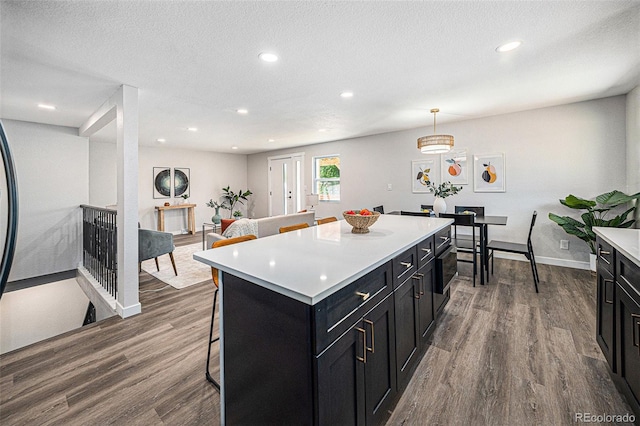 6032 Estes St, Arvada, CO 80004 - kitchen with dark cabinetry, dark wood-type flooring, light countertops, a center island, and a kitchen breakfast bar