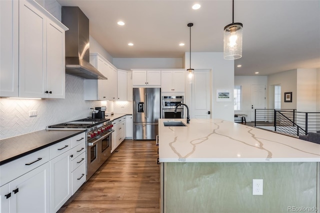 kitchen featuring a large island, stainless steel appliances, wall chimney range hood, and decorative light fixtures