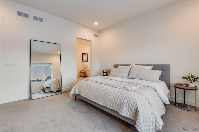 bedroom with ensuite bathroom and light colored carpet