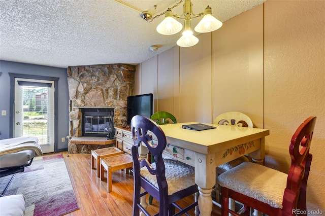 dining area with light hardwood / wood-style flooring, an inviting chandelier, a stone fireplace, and a textured ceiling