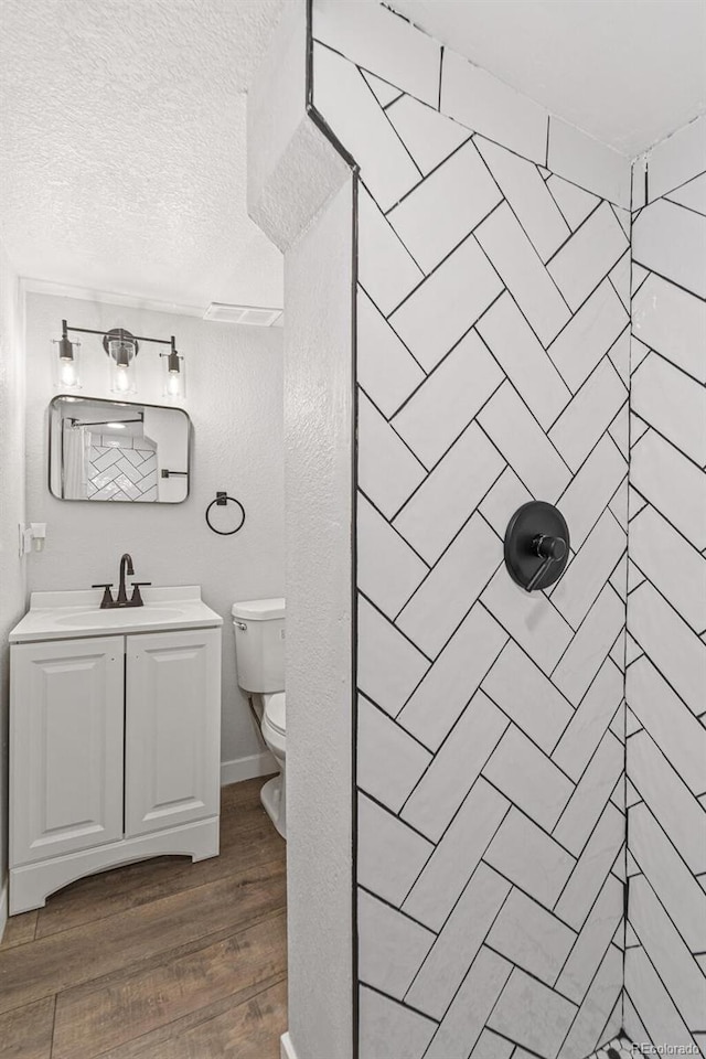 bathroom with hardwood / wood-style floors, vanity, toilet, tiled shower, and a textured ceiling