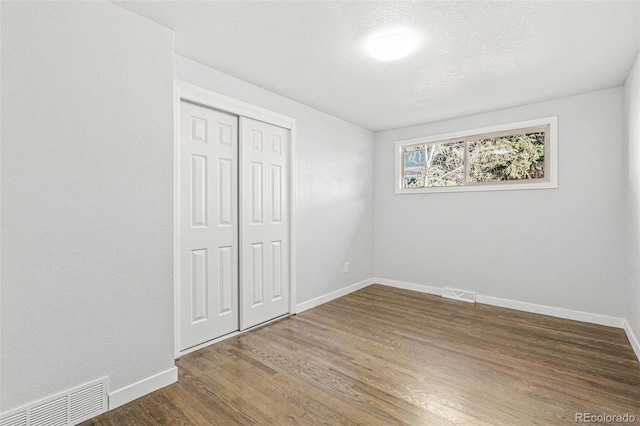 unfurnished bedroom featuring dark hardwood / wood-style flooring, a textured ceiling, and a closet