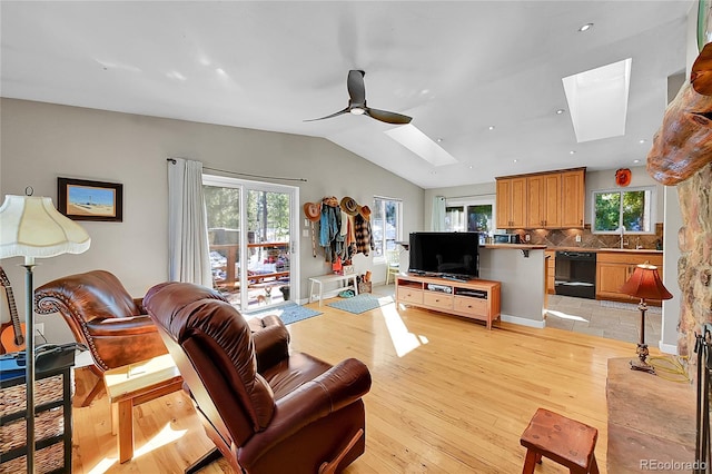 living room with ceiling fan, vaulted ceiling with skylight, a healthy amount of sunlight, and light wood-type flooring