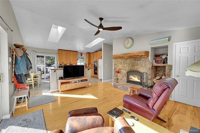 living room with a fireplace, a skylight, light hardwood / wood-style flooring, and ceiling fan