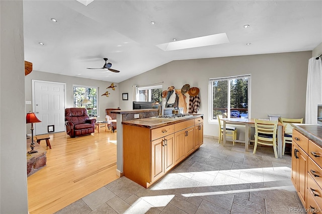 kitchen with ceiling fan, light hardwood / wood-style flooring, lofted ceiling with skylight, a kitchen island with sink, and light brown cabinetry