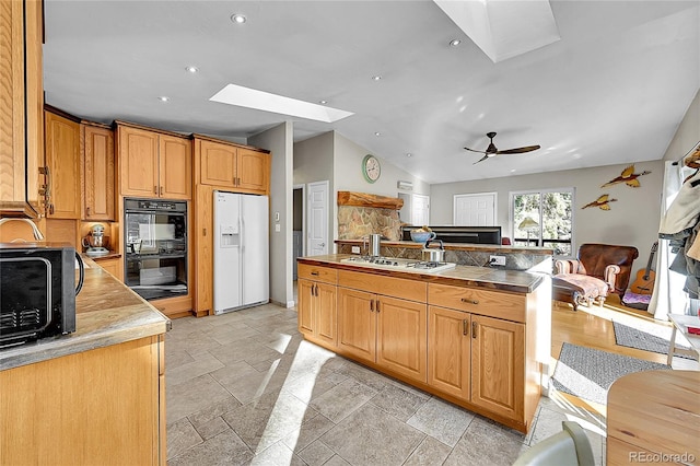 kitchen featuring stainless steel gas stovetop, black double oven, ceiling fan, white fridge with ice dispenser, and a kitchen island