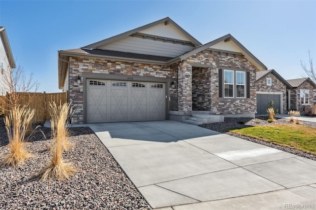 view of front facade with stone siding, driveway, an attached garage, and fence