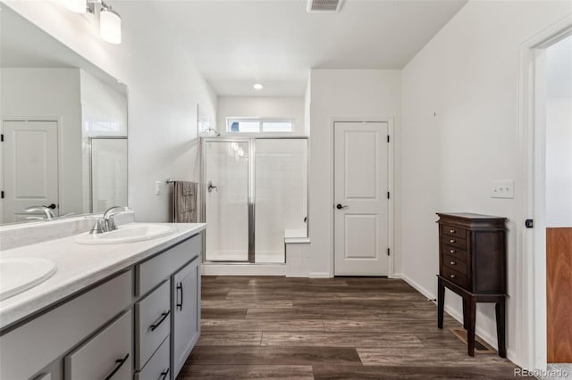 bathroom with double vanity, visible vents, a sink, a shower stall, and wood finished floors