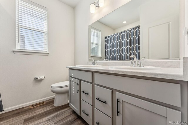 bathroom featuring double vanity, visible vents, toilet, a sink, and wood finished floors