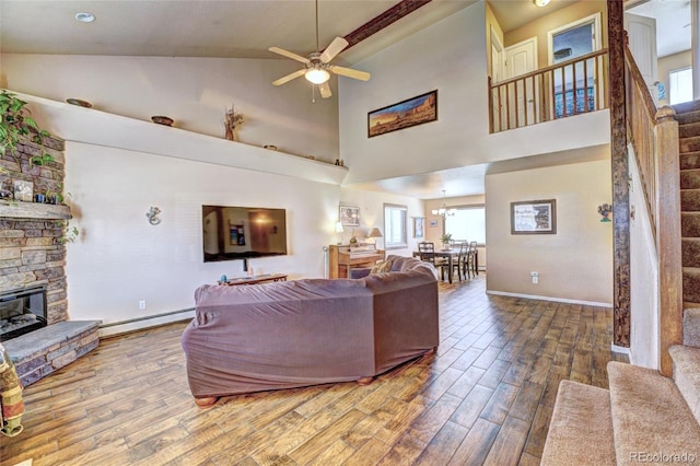 living room with high vaulted ceiling, hardwood / wood-style flooring, baseboard heating, a fireplace, and ceiling fan with notable chandelier