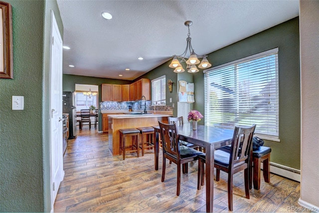 dining area featuring sink, a notable chandelier, light wood-type flooring, a baseboard radiator, and a textured ceiling