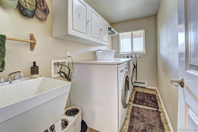 laundry area featuring washer and dryer, sink, baseboard heating, cabinets, and light hardwood / wood-style flooring