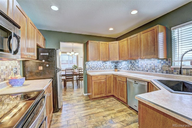 kitchen featuring appliances with stainless steel finishes, light wood-type flooring, pendant lighting, and backsplash