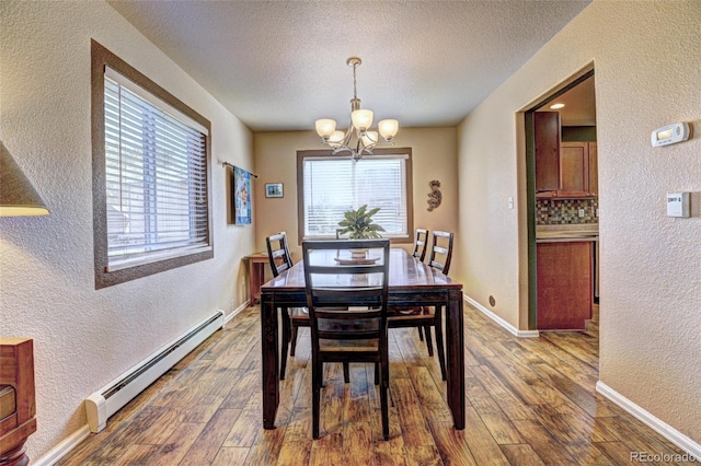 dining space featuring hardwood / wood-style flooring, a textured ceiling, a baseboard heating unit, and an inviting chandelier