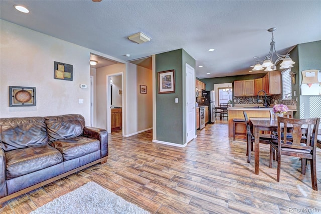 living room featuring sink, a notable chandelier, a textured ceiling, and light hardwood / wood-style floors