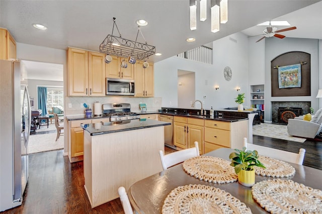 kitchen with a peninsula, light brown cabinets, dark countertops, a sink, and appliances with stainless steel finishes